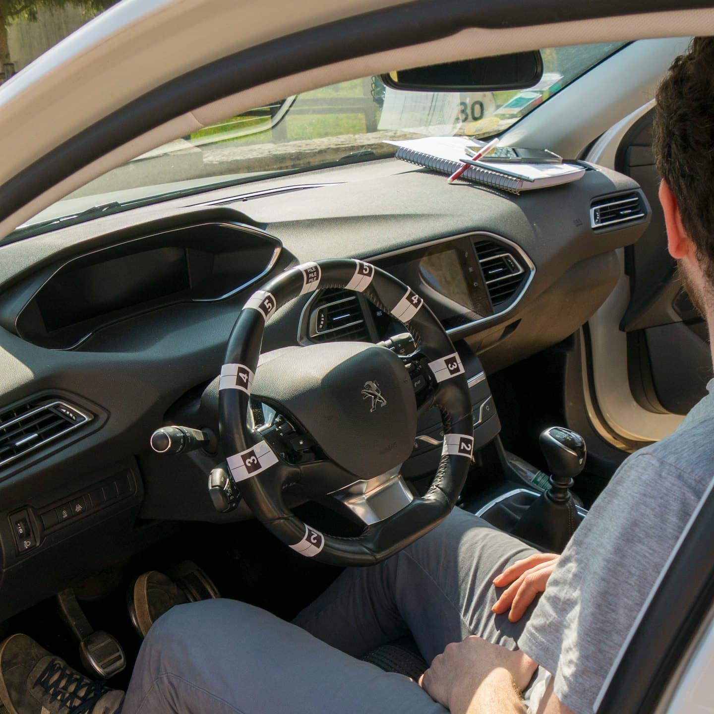 Student sitzt in einem Auto mit nummerierten Lenkradbedienelementen.